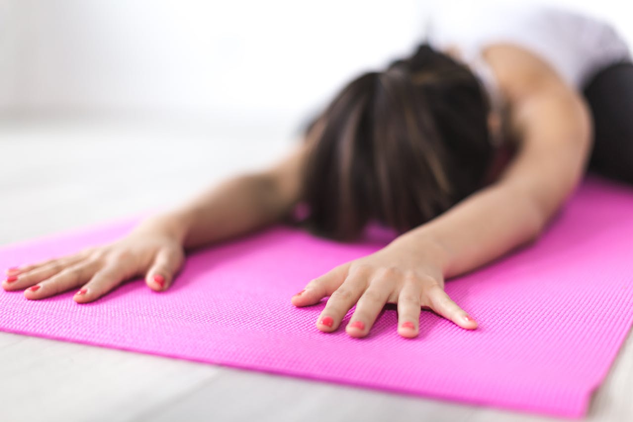 Close-up of woman stretching on a pink yoga mat, promoting relaxation and mindfulness.